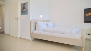 Et soveværelse med en seng, en dør, et billede og en lampe på væggen.