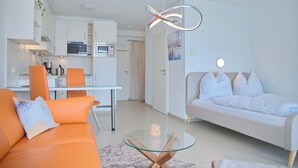 En moderne stue med sofa, sofabord i glas og et køkken i baggrunden.