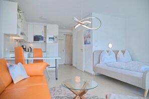 Ein modernes Wohnzimmer mit einer Couch, einem Glastisch und einer Küche im Hintergrund.