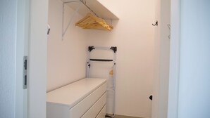 En smal gang med en hvid bænk, et tøjstativ og en metalkasse med hylder.