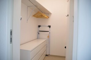 Ein schmaler Flur mit einer weißen Bank, einem Kleiderständer und einem Metallregal.