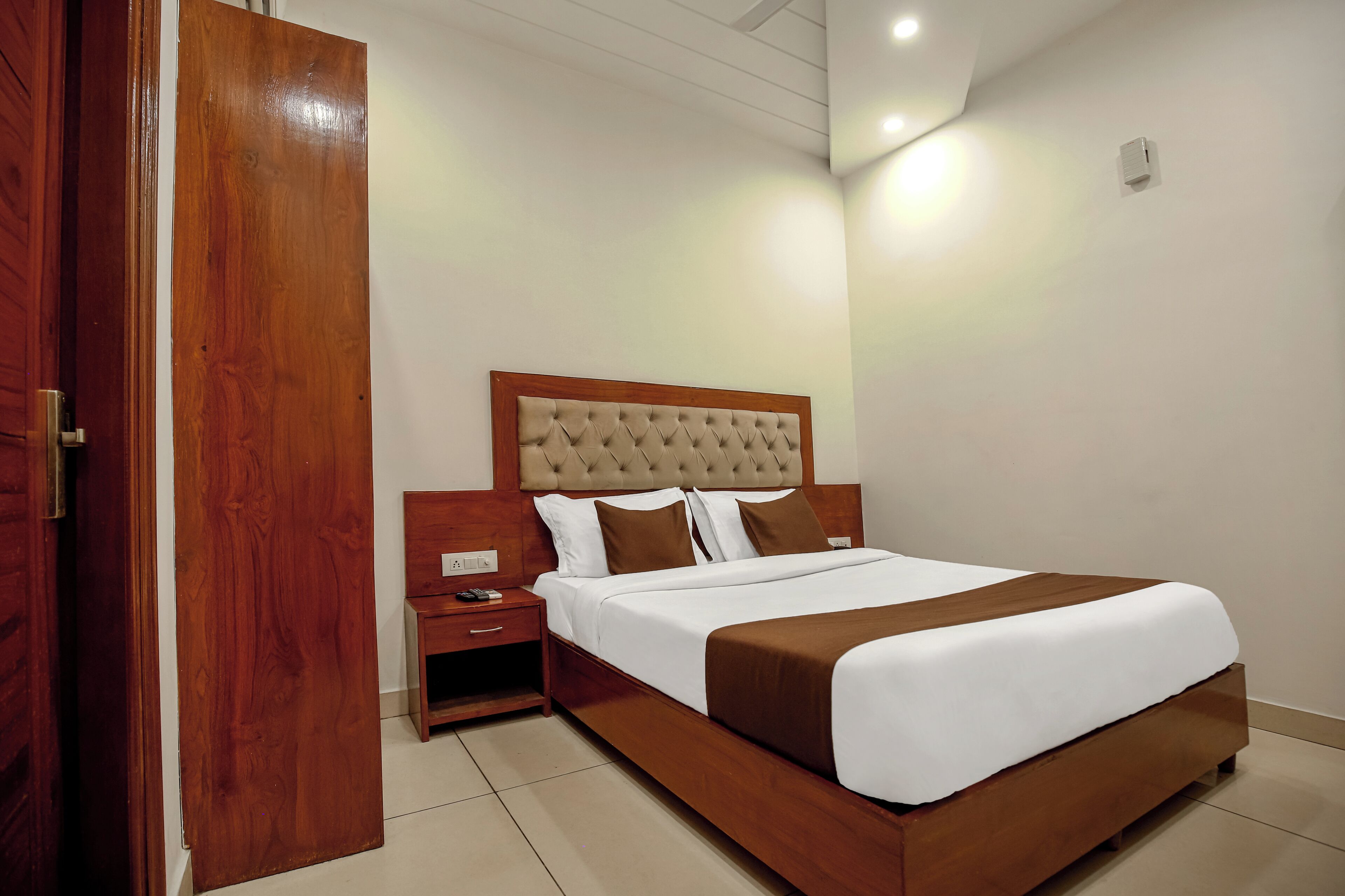 A hotel room with a wooden bed, white bedding, a nightstand, and a wooden door.