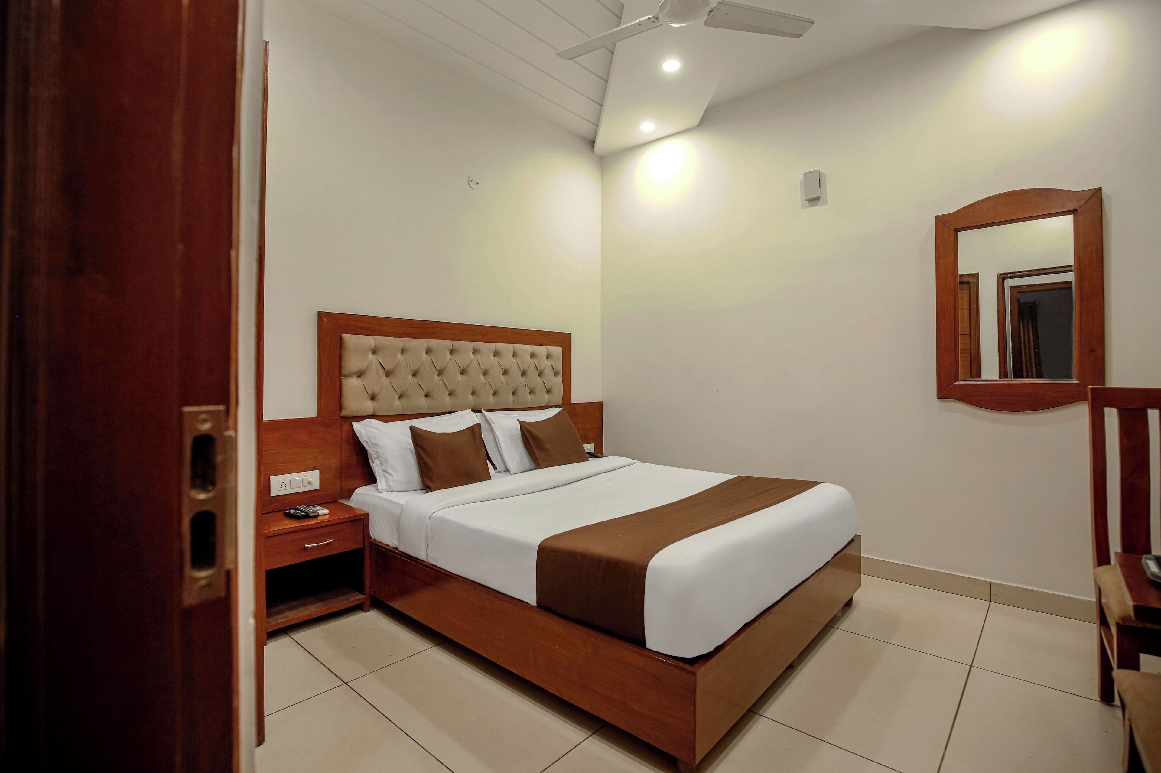 A neatly arranged hotel room with a wooden bed frame, a bedside table, a nightstand, and a mirror on the wall.