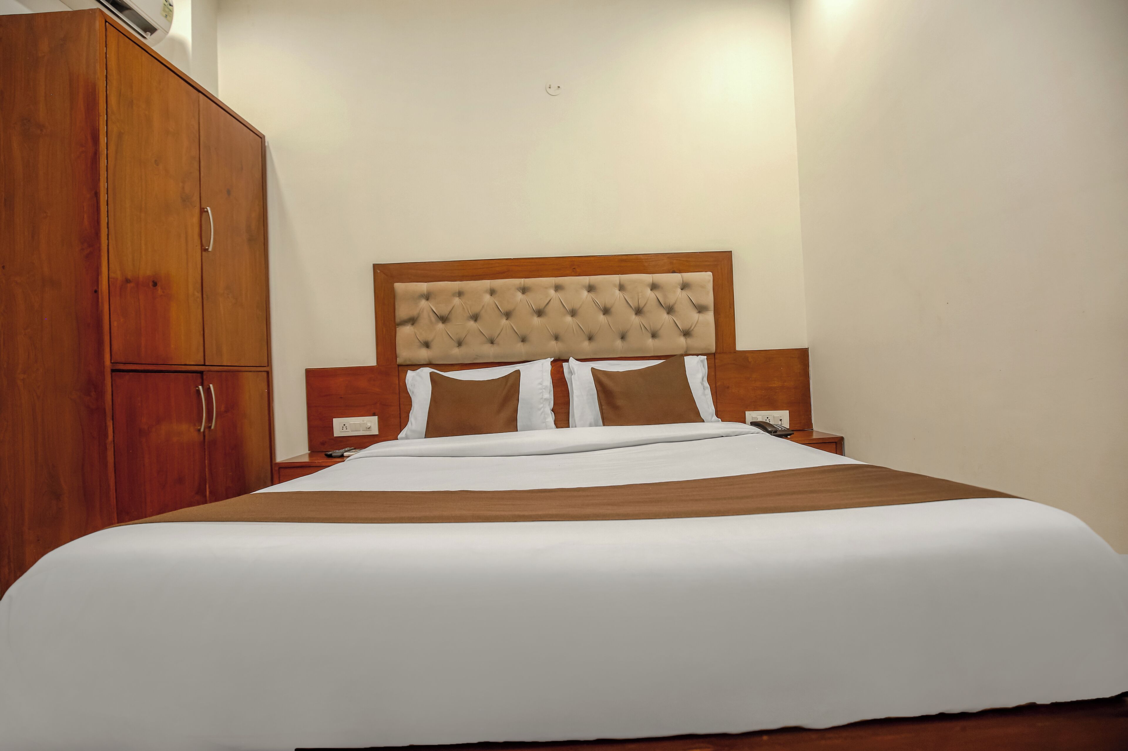 A hotel room with a large bed, wooden wardrobe, and a tufted headboard.