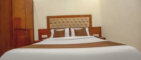A hotel room with a large bed, wooden wardrobe, and a tufted headboard.