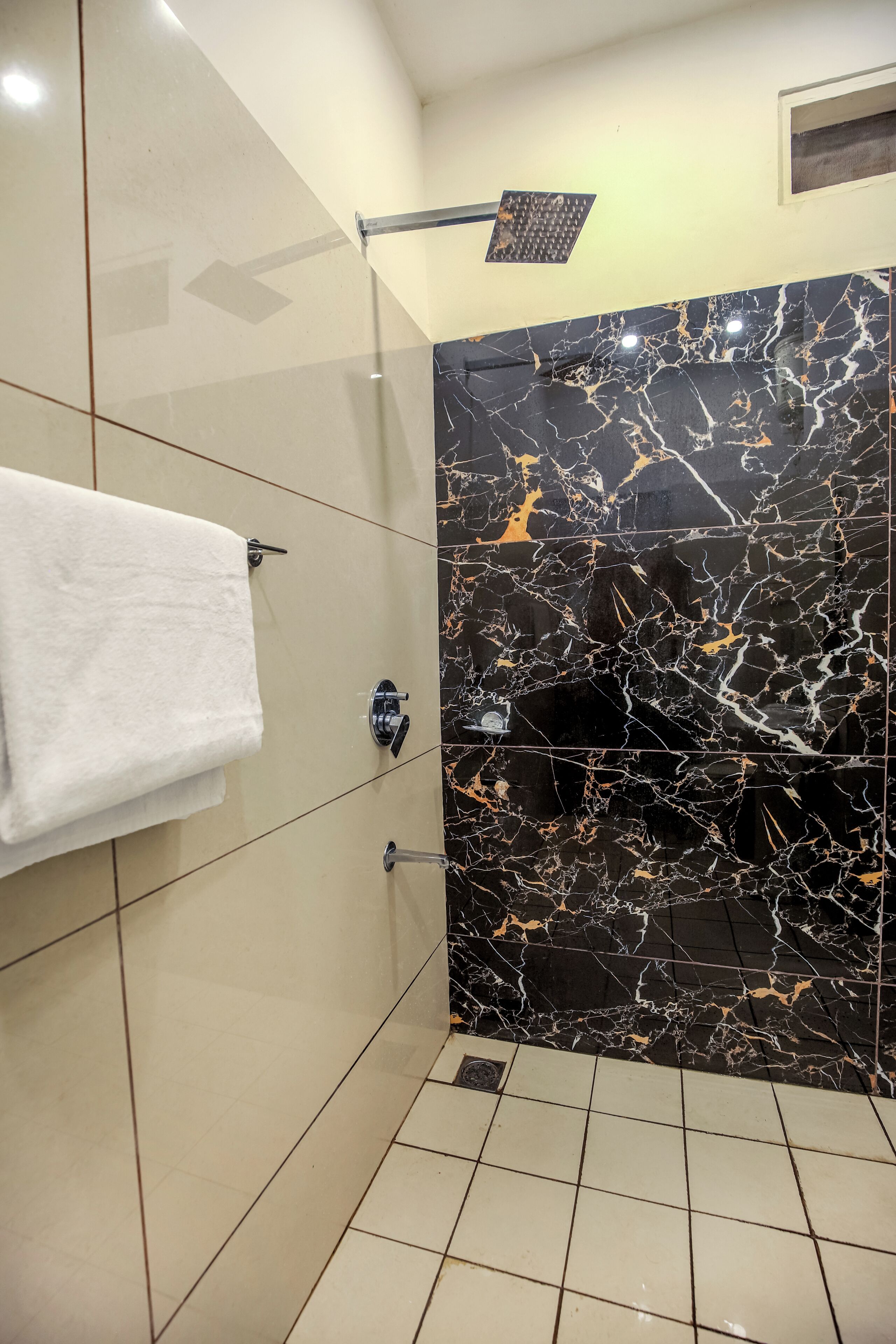 Ein modernes Badezimmer mit schwarzer Marmorwand in der Dusche, einem weißen Handtuch auf einem Halter und einer sichtbaren Duschbrause.