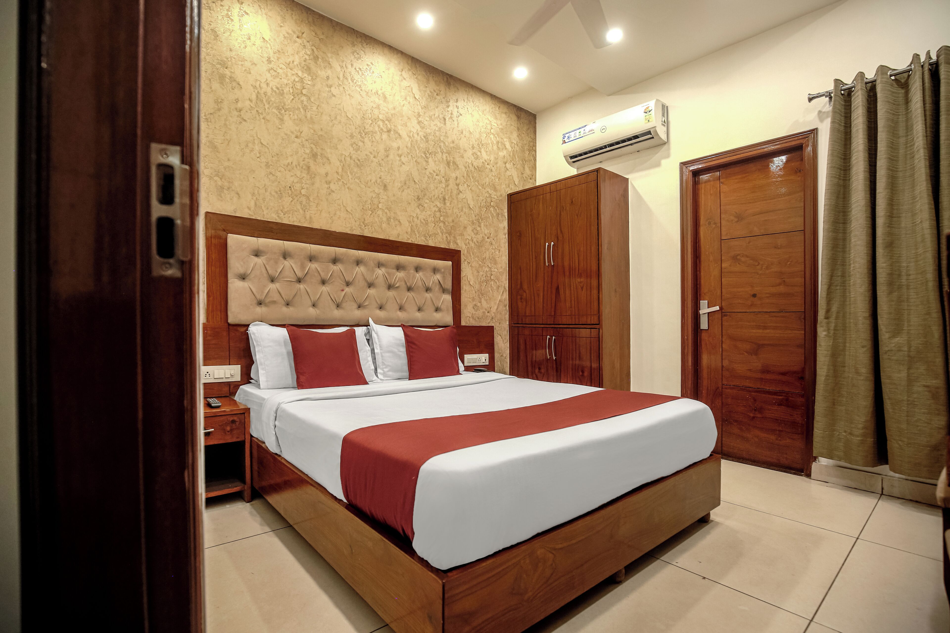 A hotel room with a large bed, wooden wardrobe, and an air conditioning unit on the wall.