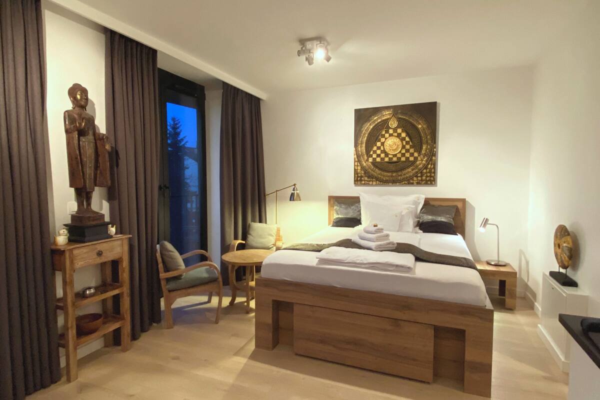A modern hotel room with a large bed, a desk, a chair, and a statue.