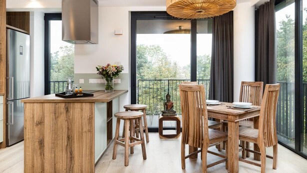 A modern kitchen with a wooden island, bar stools, and a dining table with chairs. - Araliya (Kraków)
