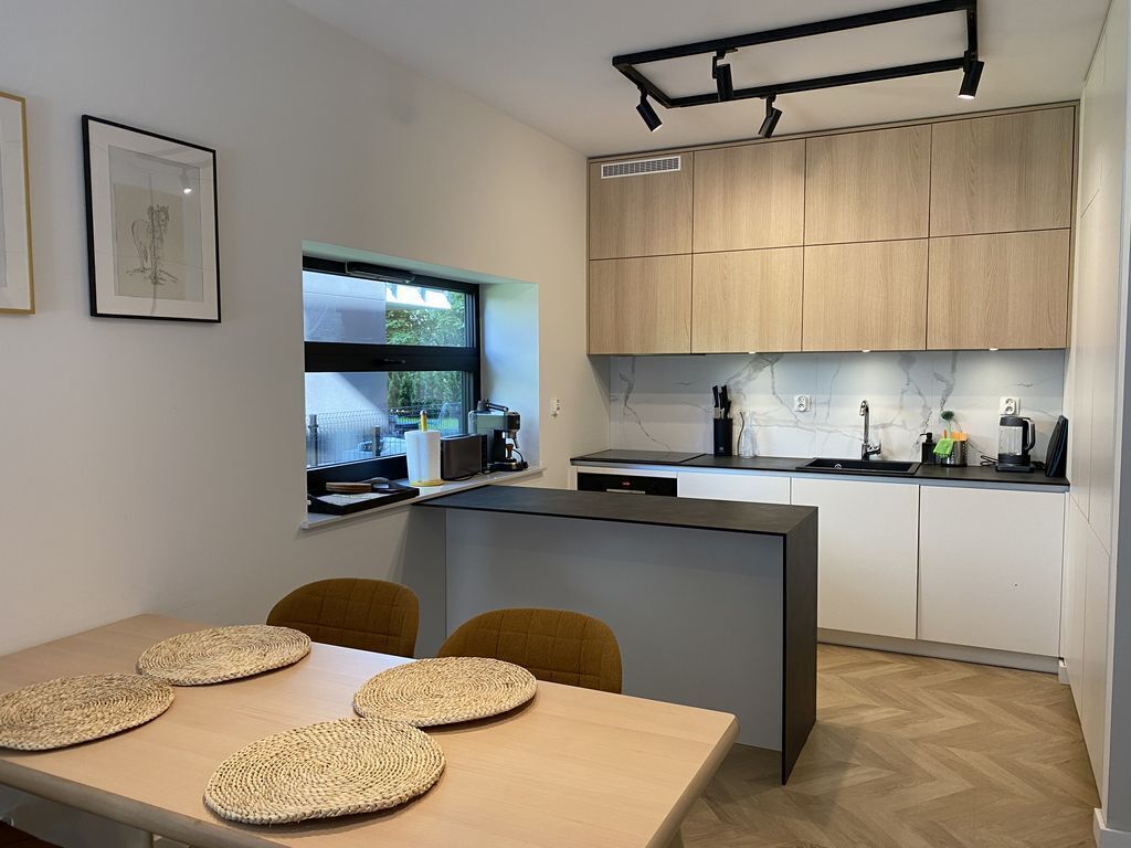 Une cuisine moderne dotée d’un îlot central, de meubles en bois et d’une fenêtre donnant sur un espace verdoyant.