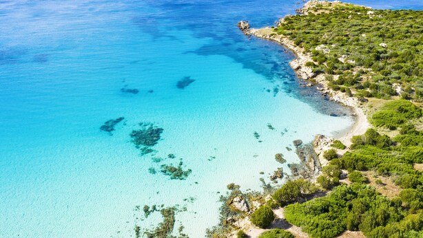 Vue aérienne d’une zone côtière avec des eaux turquoise limpides, une plage de sable et une végétation verdoyante et luxuriante.