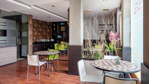 A modern dining area with round tables and chairs, a decorative wall with a floral pattern, and a wooden floor. - Tripletree Majestiq Hotel (Pekanbaru)