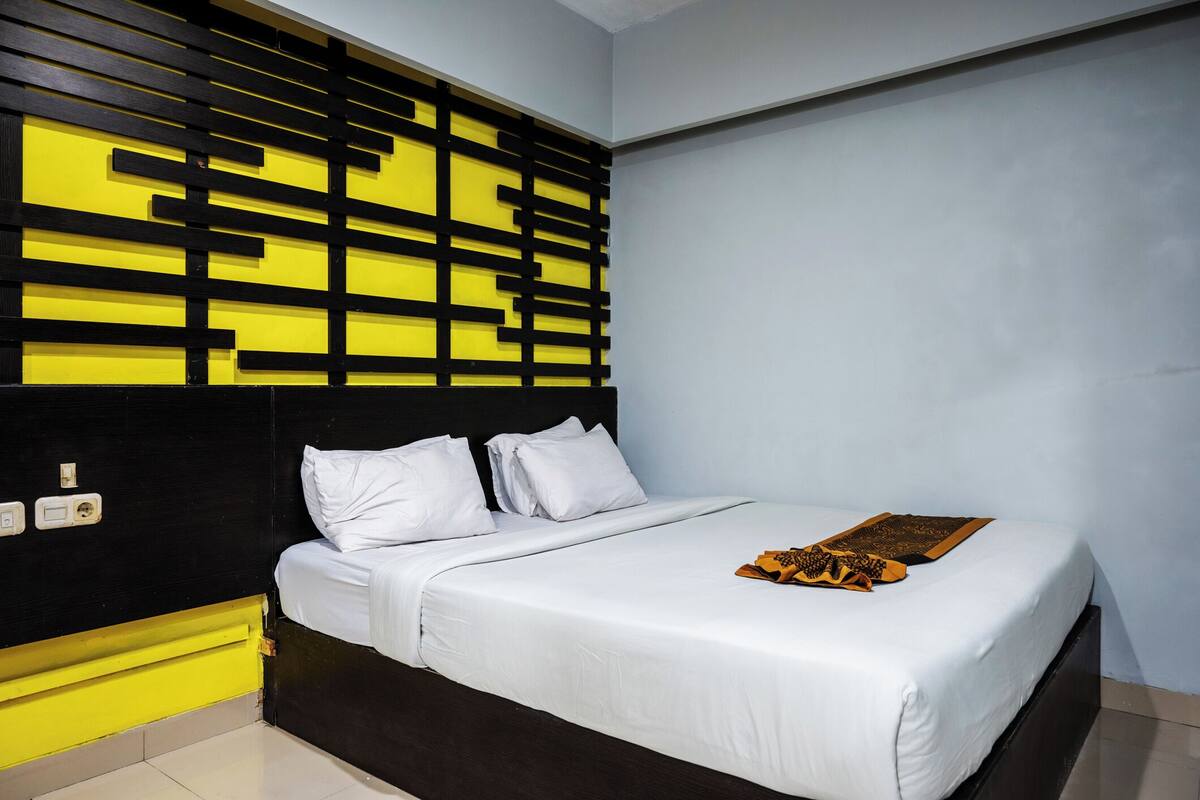 Una habitación de hotel con cama, ropa de cama blanca, cabecero negro y un panel de pared amarillo y negro.