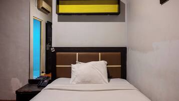 A single bed with a headboard, a bedside table with a phone, and a wall-mounted shelf above the bed.