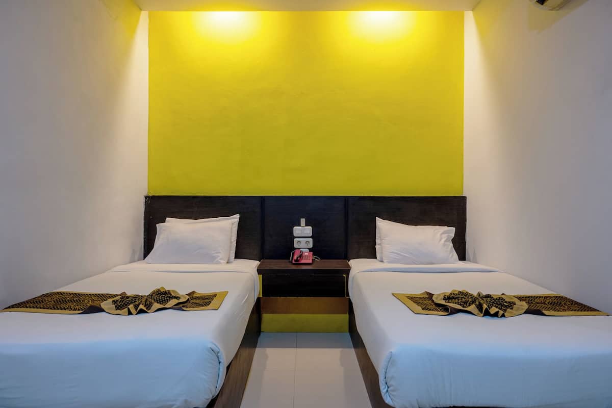Habitación de hotel con dos camas, una mesita de noche con teléfono y una pared de acento amarillo brillante.