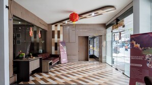 A hotel reception area with a checkered floor, a reception desk, a seating area, and a large poster advertising massage services. - Tripletree Majestiq Hotel (Pekanbaru)