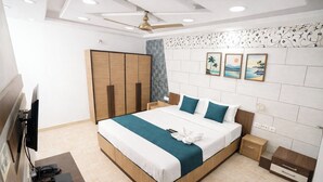 A modern hotel room with a large bed, wooden wardrobe, ceiling fan, and artwork on the wall. - BLESSINGS SELECT PERIAMET (Chennai)