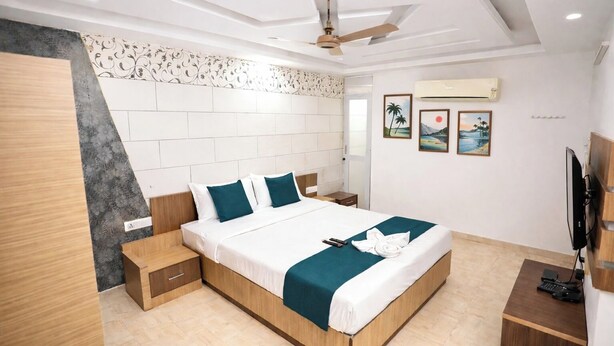 A modern hotel room with a large bed, wooden headboard, and a flat-screen TV. - BLESSINGS SELECT PERIAMET (Chennai)
