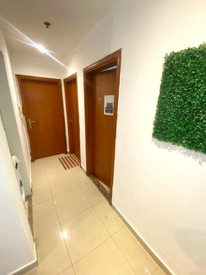 A hallway with two wooden doors, a green wall feature, and a tiled floor. - Nicest Partition Room in Tecom  (Dubai)