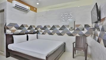 A hotel room with a bed, a chair, an air conditioning unit, a television, and a decorative wall.