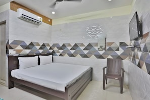 A hotel room with a bed, a chair, an air conditioning unit, a television, and a decorative wall.