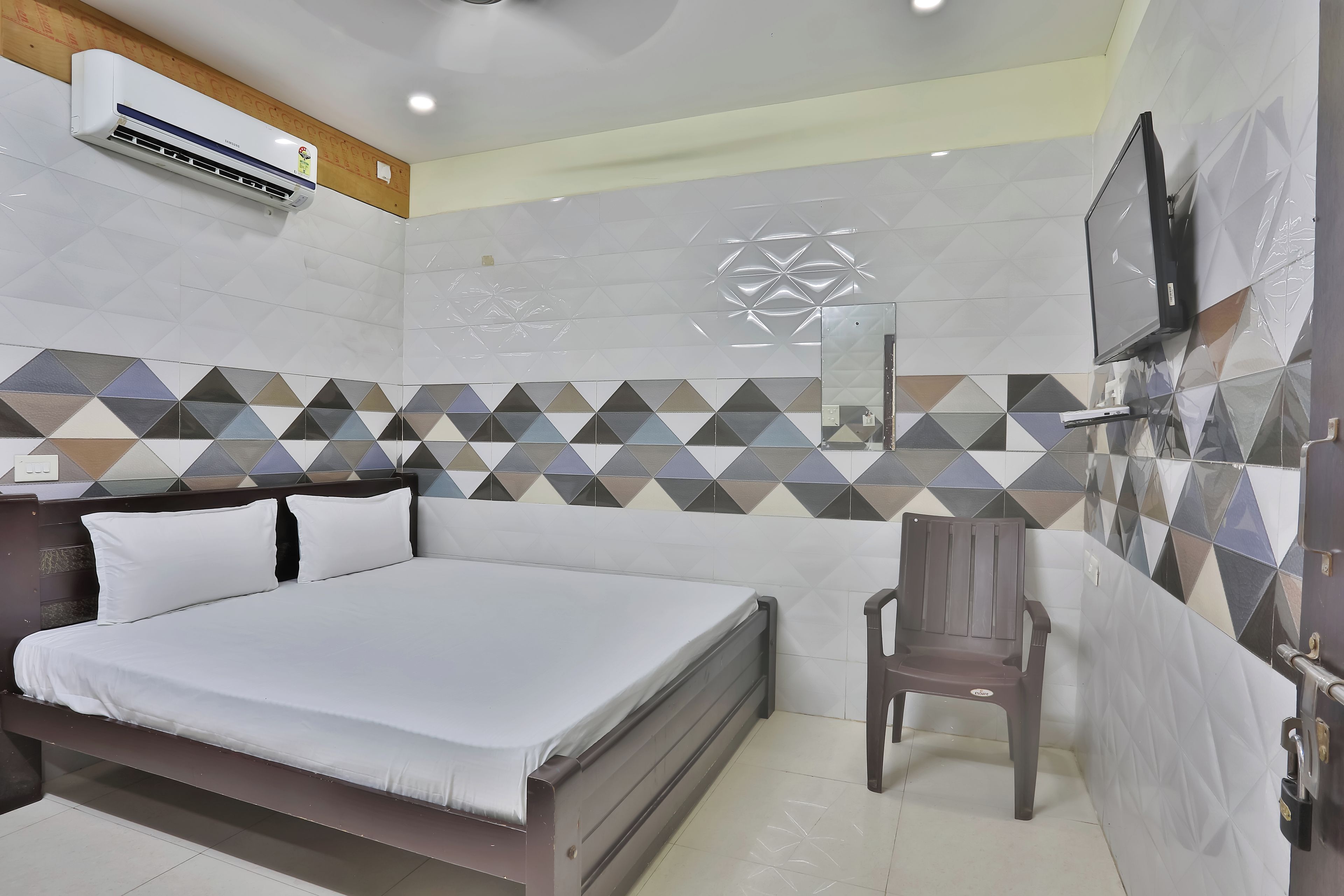 Een hotelkamer met een bed, een stoel, een televisie en een airconditioning.
