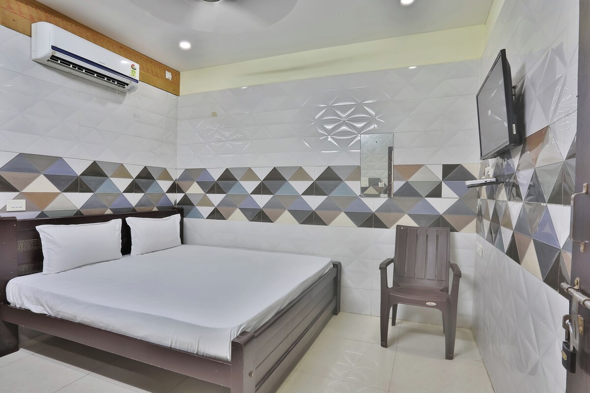 A hotel room with a bed, a chair, a TV, and an air conditioning unit.