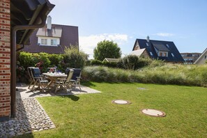 Ein Wohnhaus mit gepflegtem Rasen, einer Terrasse mit Gartenmöbeln und einer Ziegelmauer.