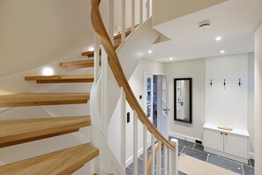 A modern staircase with wooden steps and white railings, leading to a room with a tiled floor and a white cabinet with a mirror above it. - Exclusive vacation home Dünenhafer with sauna, sea view and direct proximity to the beach (List auf Sylt)