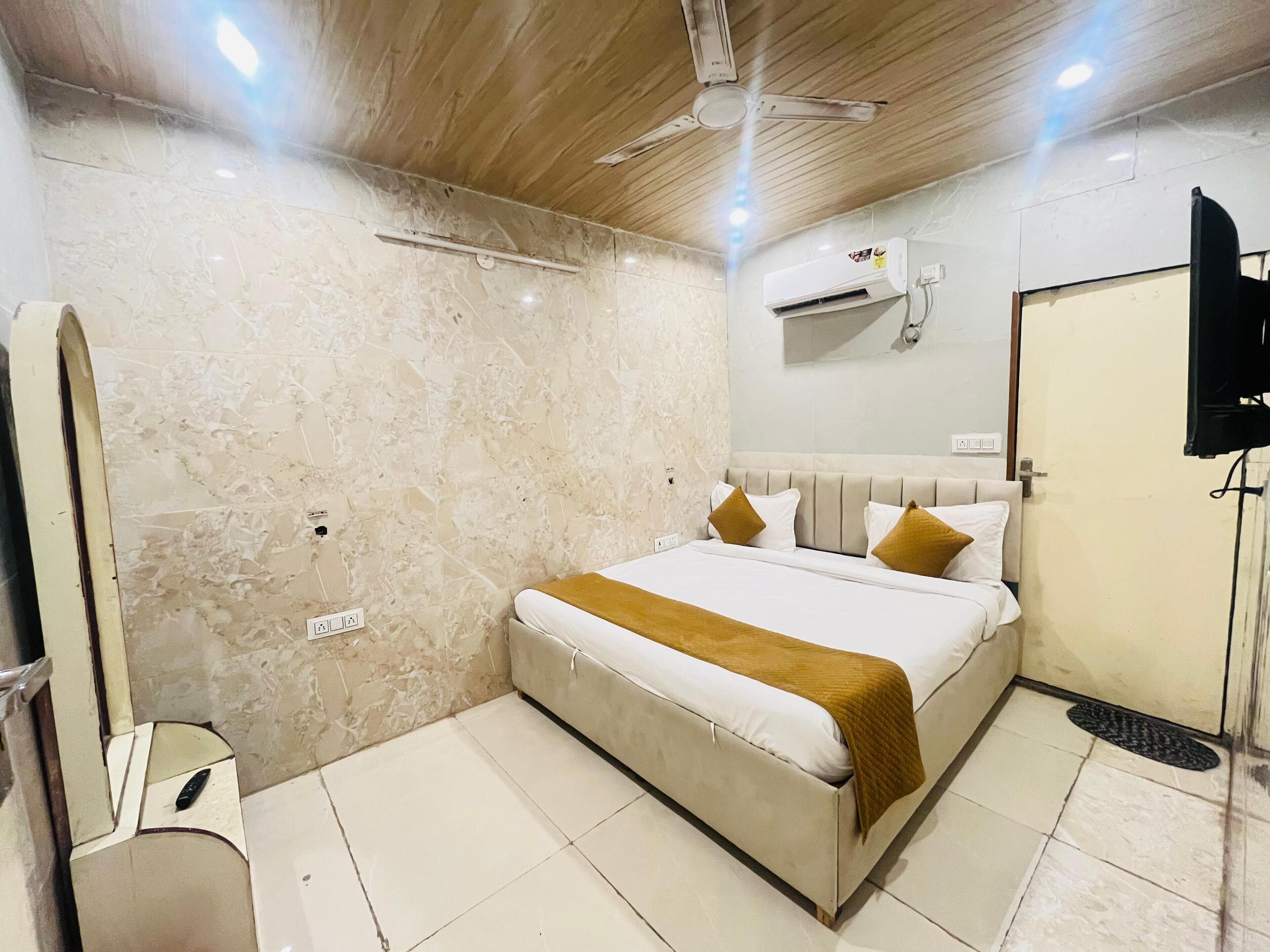 A hotel room with a bed, a ceiling fan, an air conditioning unit, a TV, and a mirror.