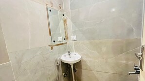 A bathroom with a white sink, a mirror, a toilet, and a blue basin. - Roomshala Hotel Golden Residency  (New Delhi)
