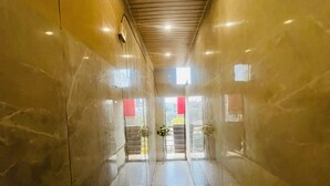 A corridor with a polished floor, a ceiling with recessed lighting, and a door at the end with a red sign. - Roomshala Hotel Golden Residency  (New Delhi)