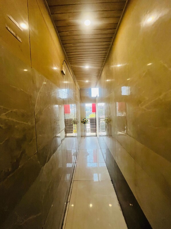 A corridor with a polished floor, a ceiling with recessed lighting, and a door at the end with a red sign.