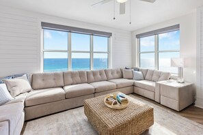 Una sala de estar moderna con un amplio sofá modular, una mesa de centro tejida y vistas al océano.