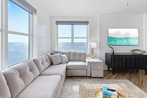 Una sala de estar moderna con un sofá modular, un televisor de pantalla plana, un mueble de madera oscura y un ventanal con vistas al océano.