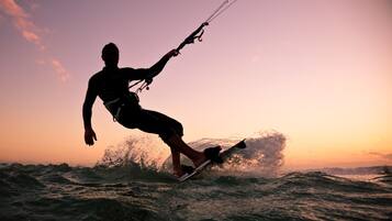 Eine Silhouette einer Person, die im Windsurfunterricht steht, vor einem Sonnenuntergang.