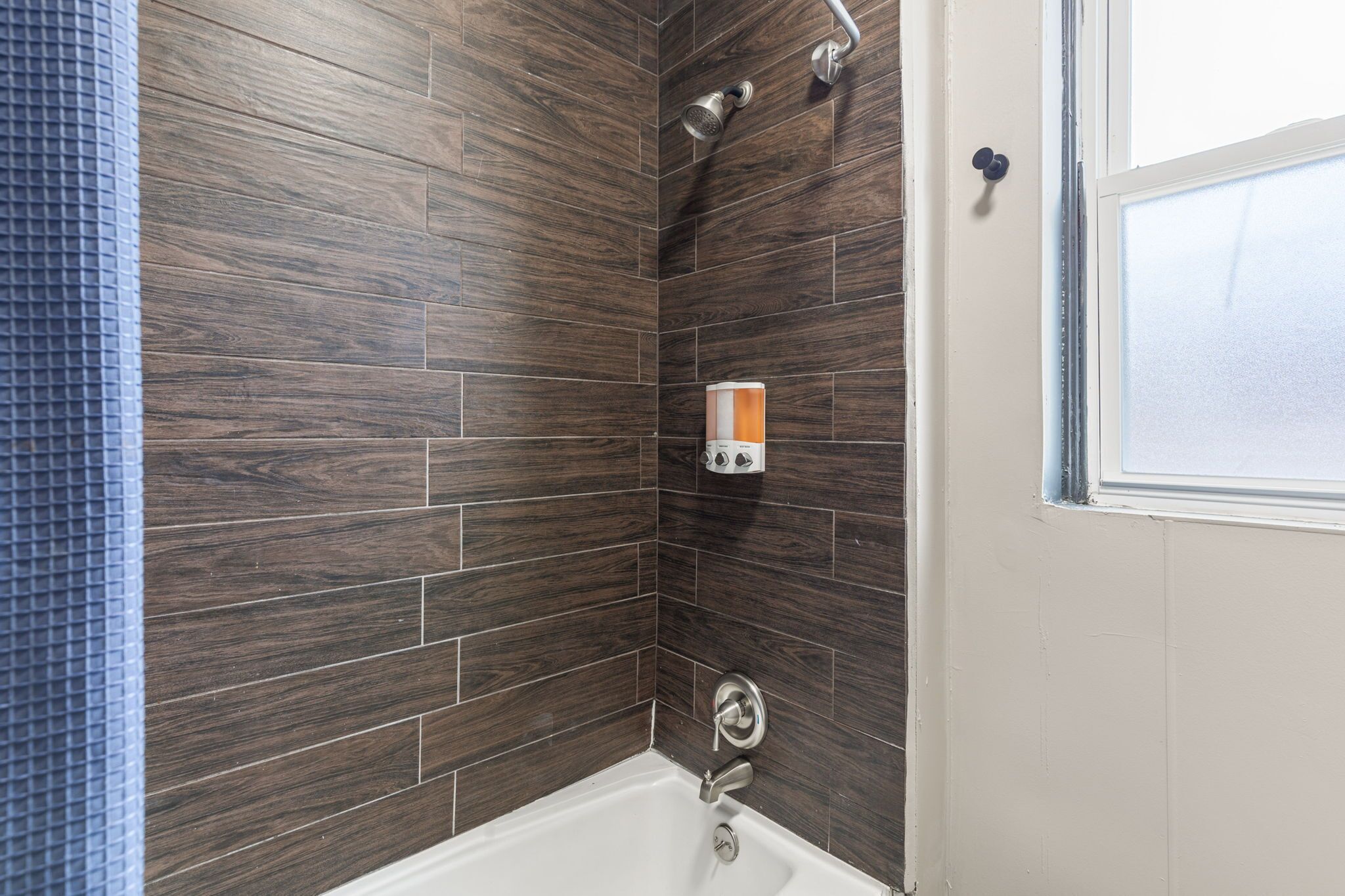 The bathroom's tub-and-shower combination features dark wood-look tile, modern fixtures, and a bright window.