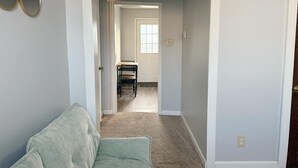 Een kamer met een lichtgroene bank, een houten eettafel met stoelen, en een deur naar een andere ruimte.