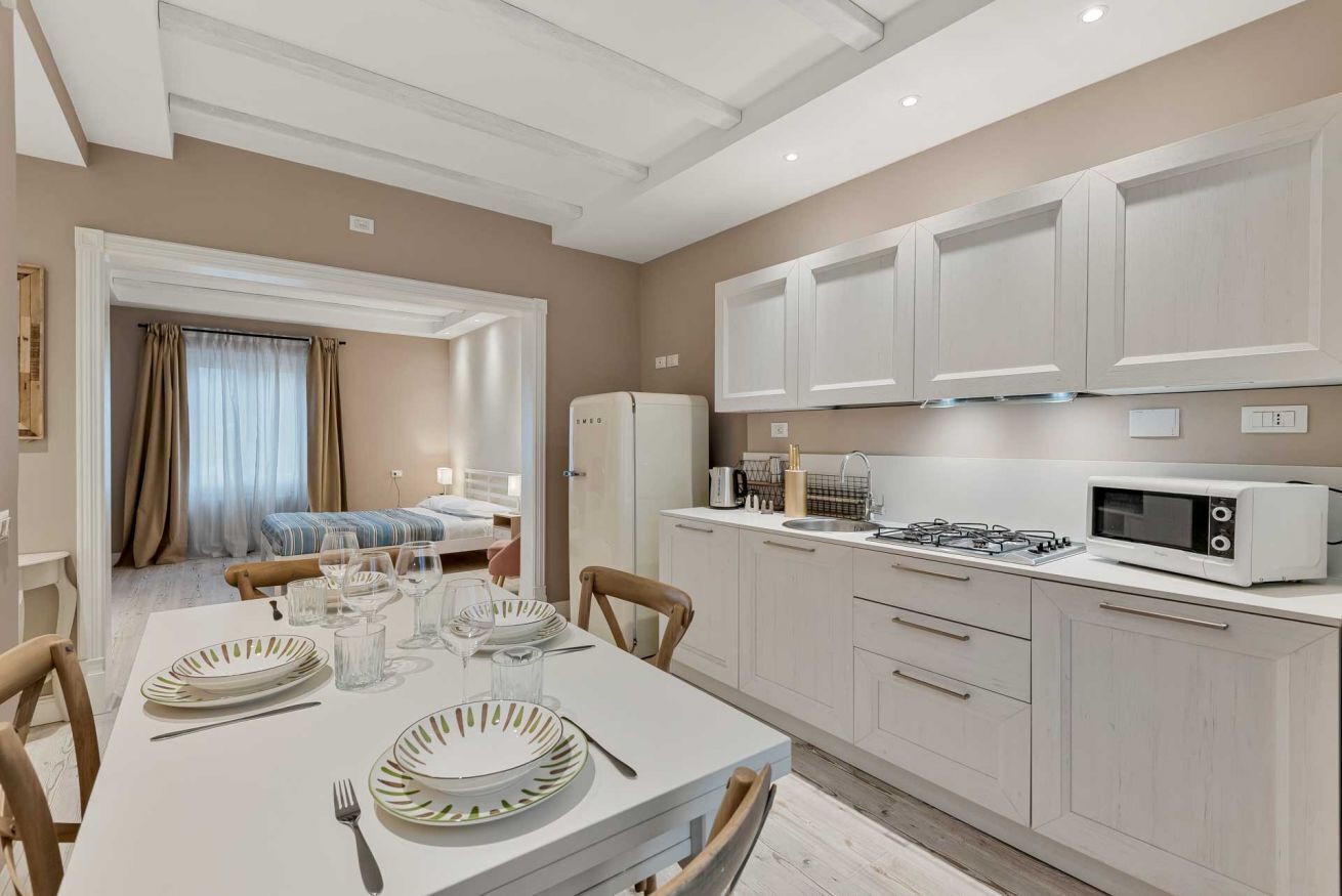 A modern kitchen with white cabinets, a microwave, and a gas stove. There is a dining table set with plates and glasses.