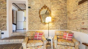 A room with a brick wall, a mirror, two floral-patterned sofas with cushions, a small table, and a refrigerator in the background.