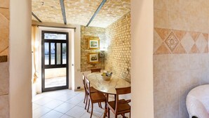A room with a stone wall, a tiled floor, a wooden dining table with chairs, and a door leading outside.