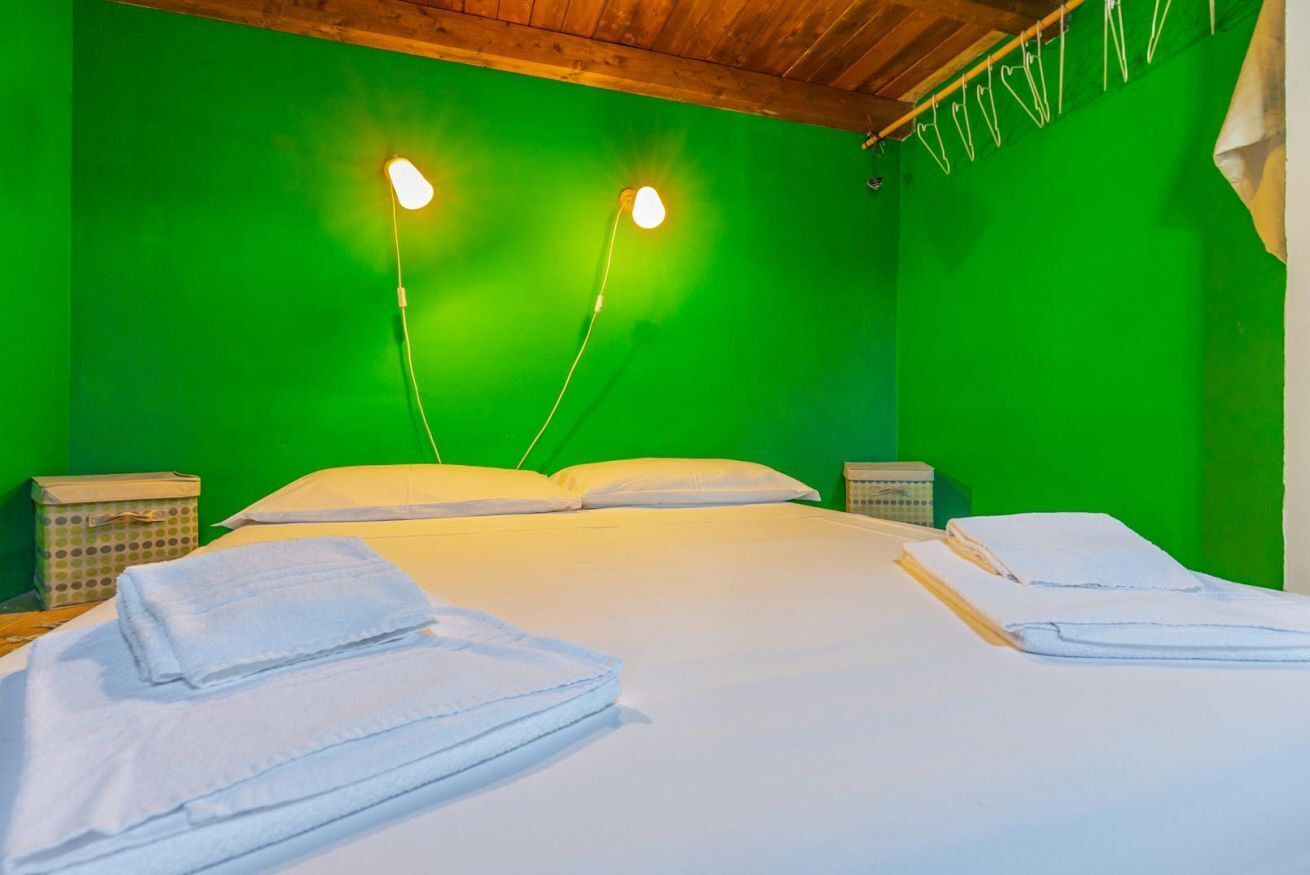 Une pièce avec un mur vert, un plafond en bois, un lit avec une literie blanche, deux tables de chevet et un écran vert.