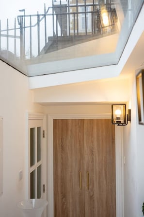 A modern interior with a wooden door, a glass balcony, and a wall-mounted light fixture. - Trendy Hoxton, Full Kitchen, Large Garden (London)