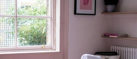A bedroom with a bed, a window, a radiator, a shelf with books, and a framed motivational poster.