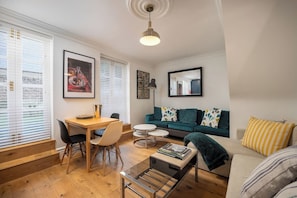 A modern living room with a wooden dining table, a sofa, and a coffee table. - Trendy Hoxton, Full Kitchen, Large Garden (London)