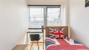 Ett sovrum med en säng som har en kudde med Union Jack-mönster, ett skrivbord med en stol och ett fönster med persienner.
