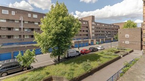En flervåningsbyggnad med bostäder, ett parkeringsområde, ett träd och en vit skåpbil som står parkerad på gatan.