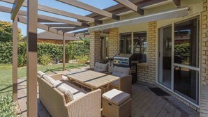 Un patio al aire libre con mobiliario de mimbre, una parrilla y una estructura de pérgola.