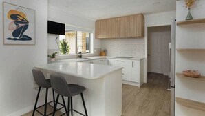 Una cocina moderna con una isla blanca, taburetes de bar, armarios de madera y un televisor de pantalla plana.