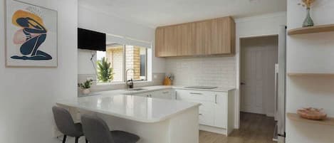 A modern kitchen with a white island, bar stools, wooden cabinets, and a flat-screen TV.